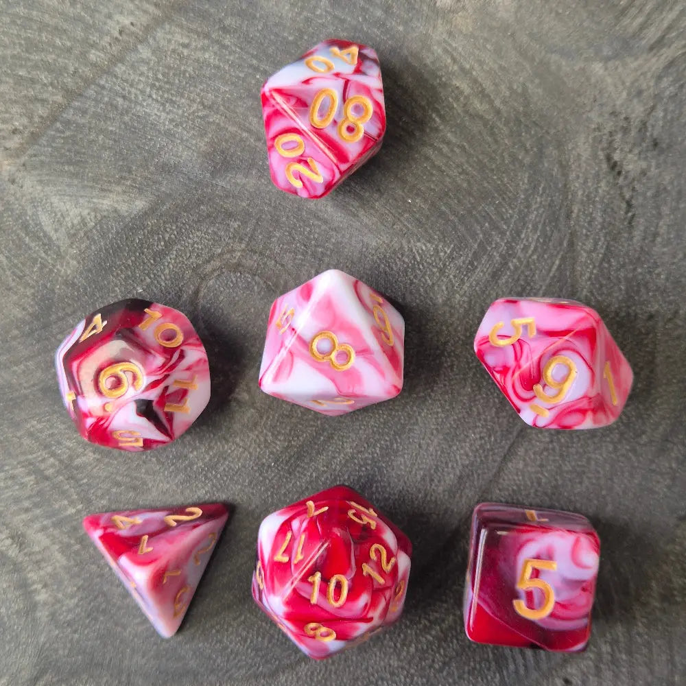 A set of red and white acrylic polymere dice with gold numbers on a wooden surface