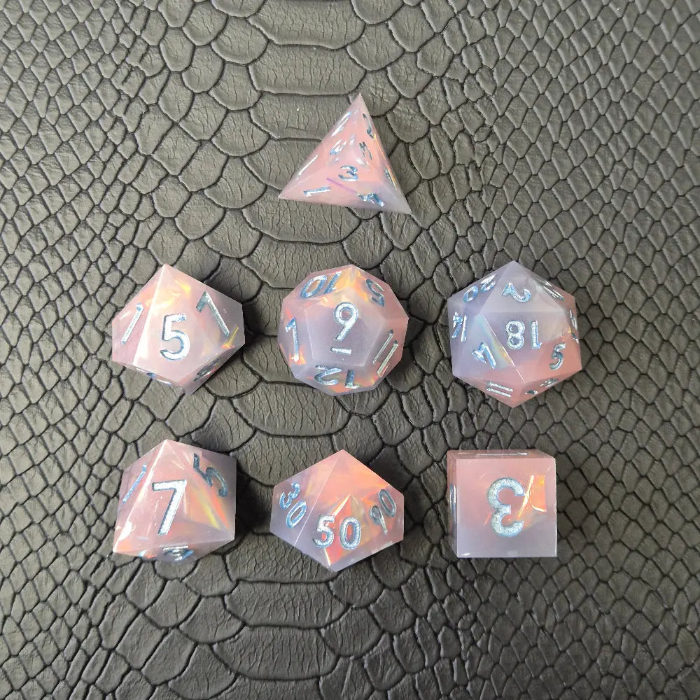 A set of pink sharp edge resin dice with blue numbers on a black textured surface