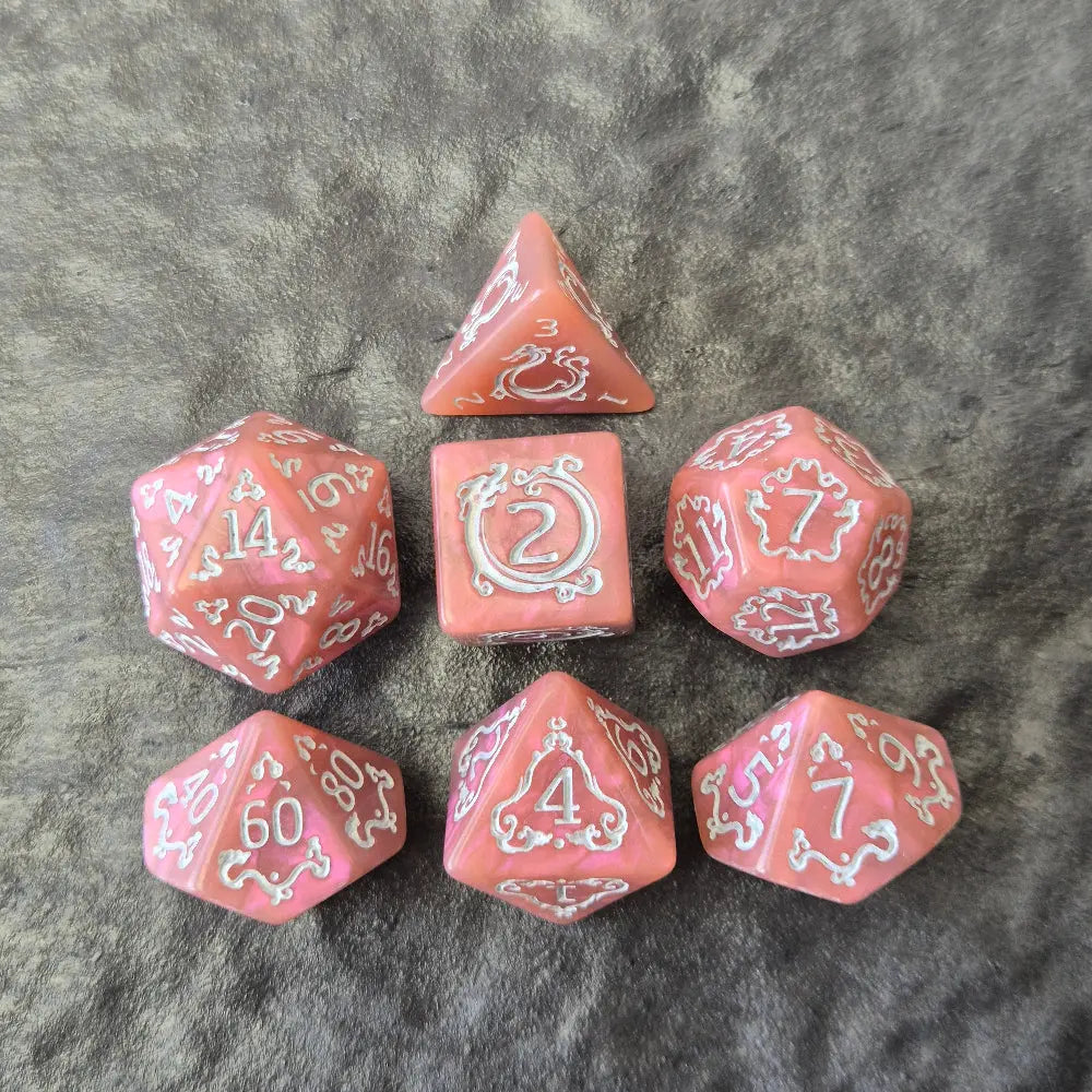 Pink acrylic D&D dice set with white arcane-style numbers and elegant swirls, displayed on a textured grey surface.