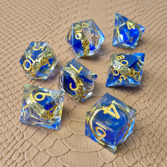 Sharp-edge polyhedral dice set with golden ring embedded in clear and blue resin, gold inked numbers, displayed on a fantasy-style textured surface.