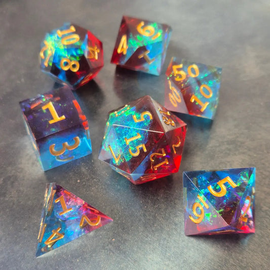 A set of red and blue translucent Sharp Edge dice with gold numbering and iridescent flecks, displayed on a metallic surface.