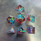 A set of red and blue translucent Sharp Edge dice with gold numbering and iridescent flecks, displayed on a metallic surface.