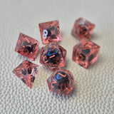 A set of red tinted clear liquid core dice with a moving dragon eye inside on a white textured background