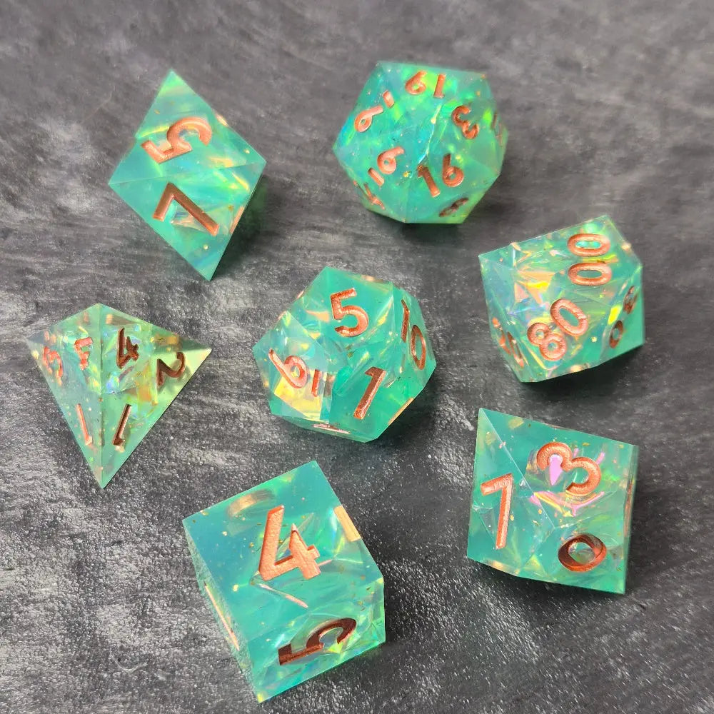 Sharp-edge polyhedral dice set with clear aqua blue resin, filled with holographic foil flakes and copper inked numbers, displayed on a black surface.