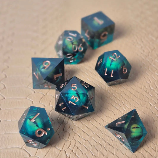 A set of clear green tinted liquid core resin dice with moving dragon eye inside and gold numbers engraved, displayed on a beige scale surface
