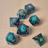 A set of clear green tinted liquid core resin dice with moving dragon eye inside and gold numbers engraved, displayed on a beige scale surface