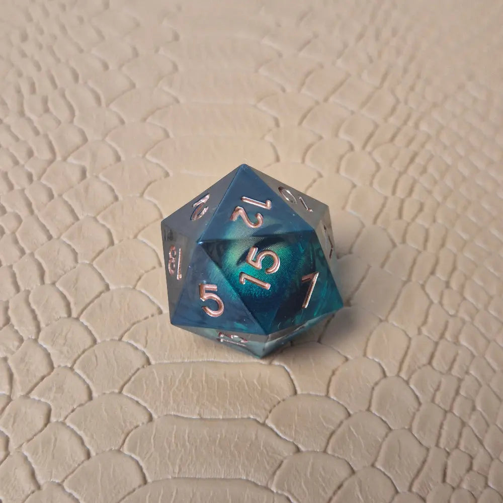 A set of clear green tinted liquid core resin dice with moving dragon eye inside and gold numbers engraved, displayed on a beige scale surface