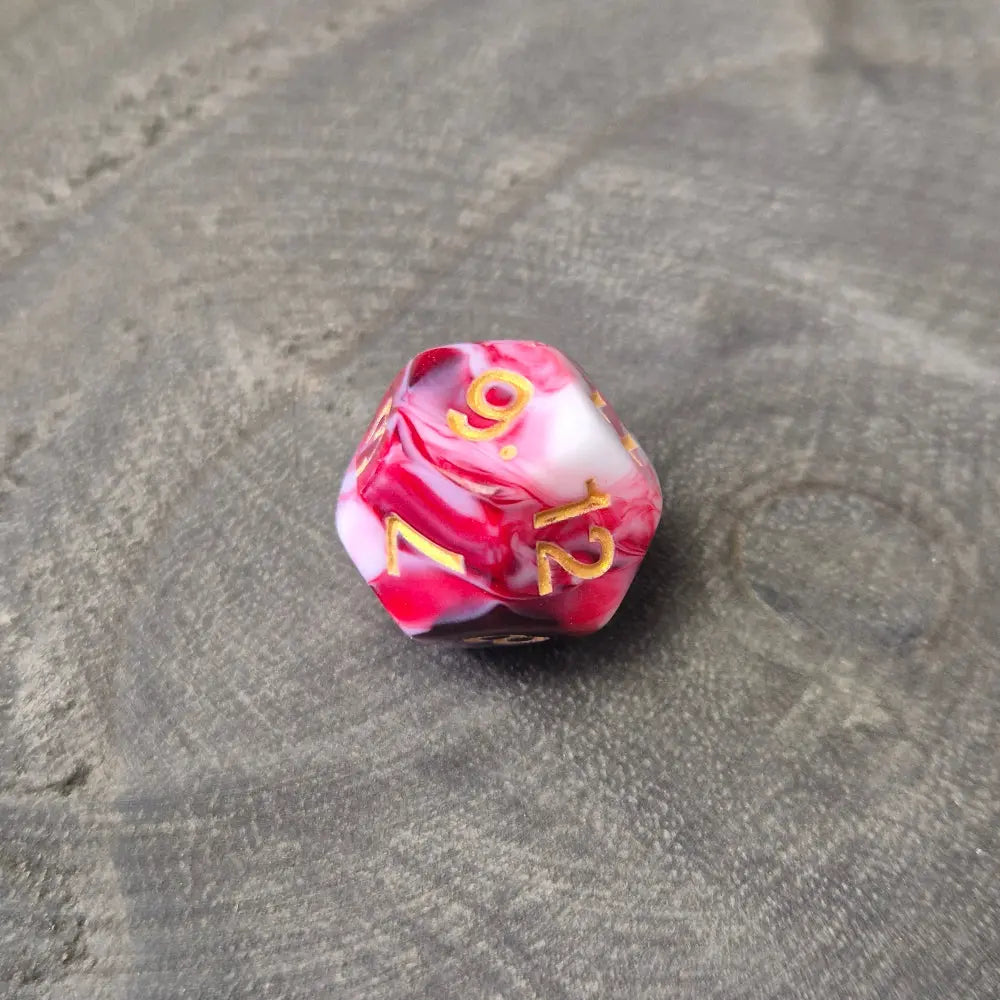 A set of red and white acrylic polymere dice with gold numbers on a wooden surface