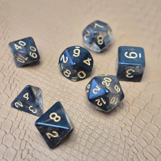 A set of clear black tinted polymere acrylic dice with gold numbers on a textured beige surface