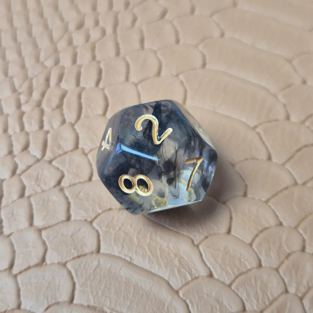 A set of clear black tinted polymere acrylic dice with gold numbers on a textured beige surface