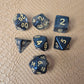 A set of clear black tinted polymere acrylic dice with gold numbers on a textured beige surface