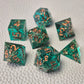 A set of turquoise tinted clear sharp edge resin dice filled with gold flakes. Displayed on a white textured surface