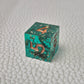 A set of turquoise tinted clear sharp edge resin dice filled with gold flakes. Displayed on a white textured surface