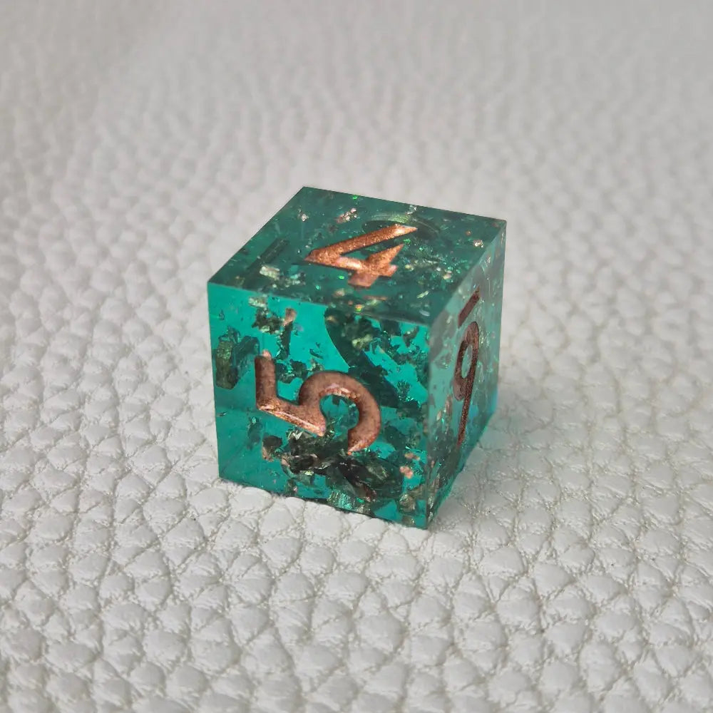 A set of turquoise tinted clear sharp edge resin dice filled with gold flakes. Displayed on a white textured surface