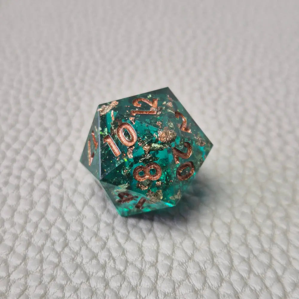 A set of turquoise tinted clear sharp edge resin dice filled with gold flakes. Displayed on a white textured surface