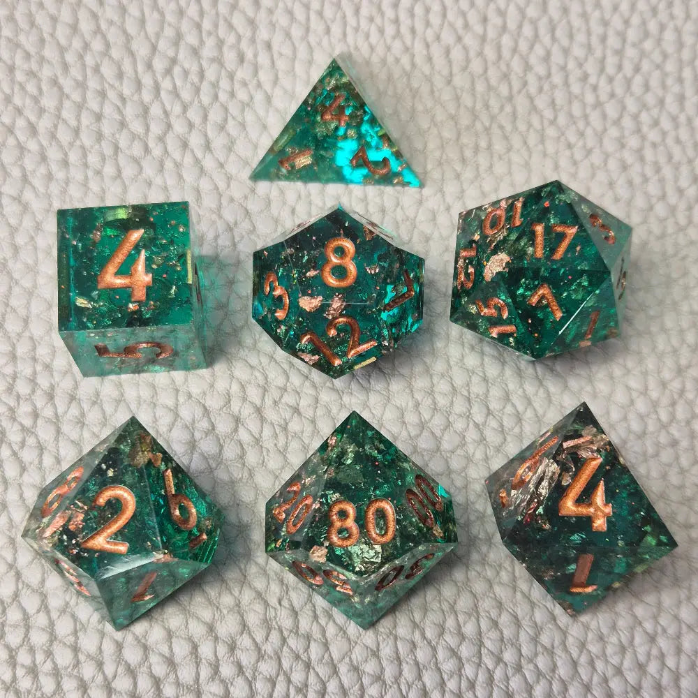 A set of turquoise tinted clear sharp edge resin dice filled with gold flakes. Displayed on a white textured surface