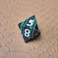 A set of black metal dice with shimmering green stripes and white numbering, displayed on a textured surface.