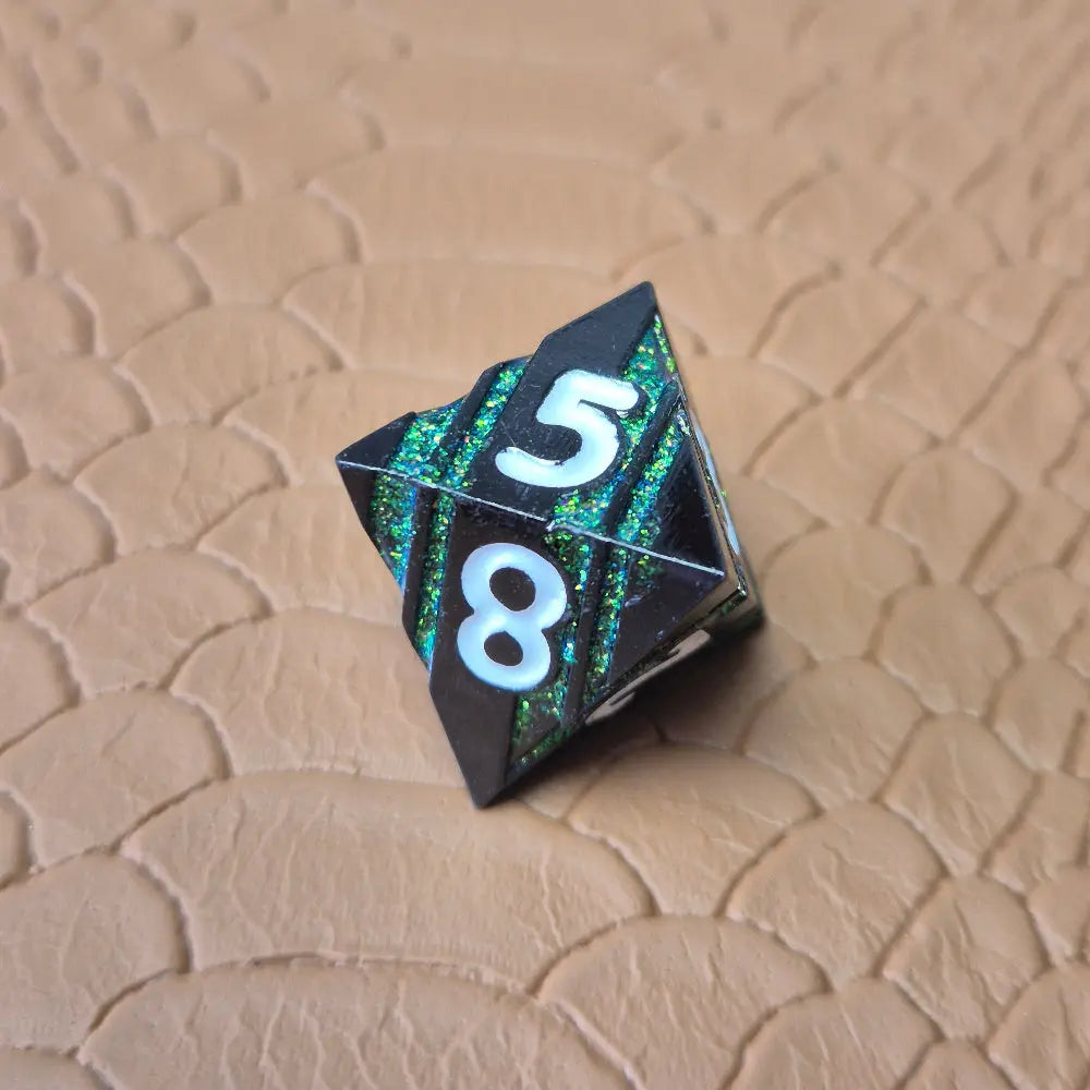 A set of black metal dice with shimmering green stripes and white numbering, displayed on a textured surface.