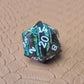 A set of black metal dice with shimmering green stripes and white numbering, displayed on a textured surface.