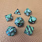 A set of black metal dice with shimmering green stripes and white numbering, displayed on a textured surface.