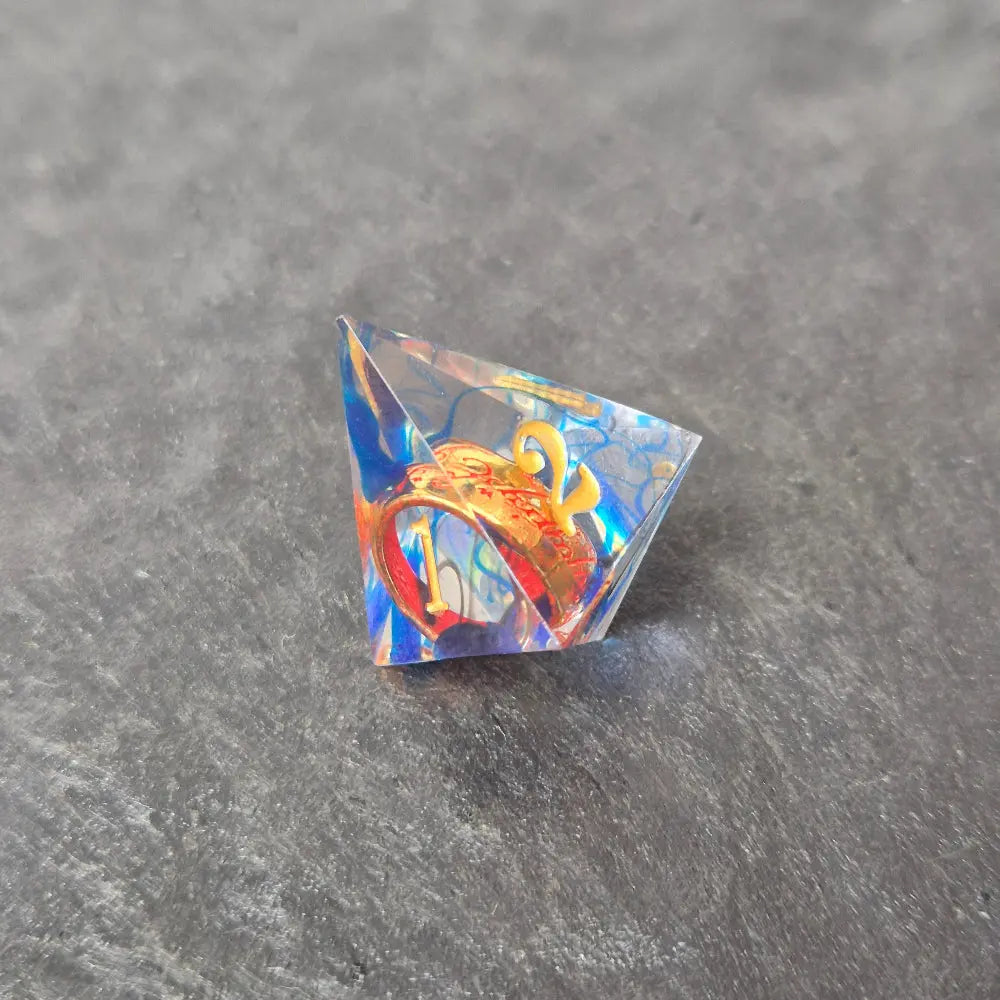 A set of clear blue tinted sharp edge resin dice with an engraved golden ring inside on a black surface