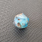 A set of clear light blue tinted liquid core dice with floating bronze flakes and white numbers, displayed on a black textured surface