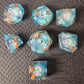 A set of clear light blue tinted liquid core dice with floating bronze flakes and white numbers, displayed on a black textured surface