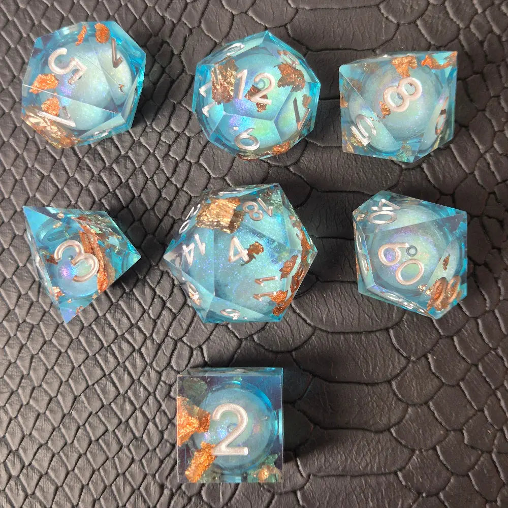 A set of clear light blue tinted liquid core dice with floating bronze flakes and white numbers, displayed on a black textured surface