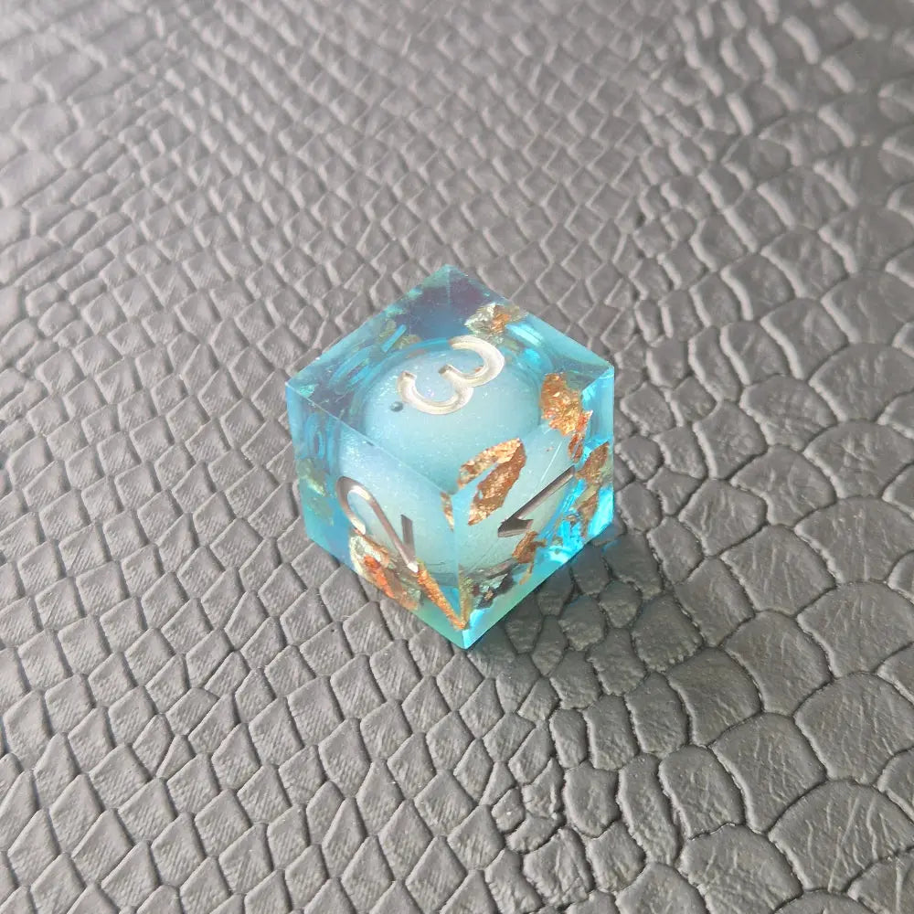 A set of clear light blue tinted liquid core dice with floating bronze flakes and white numbers, displayed on a black textured surface