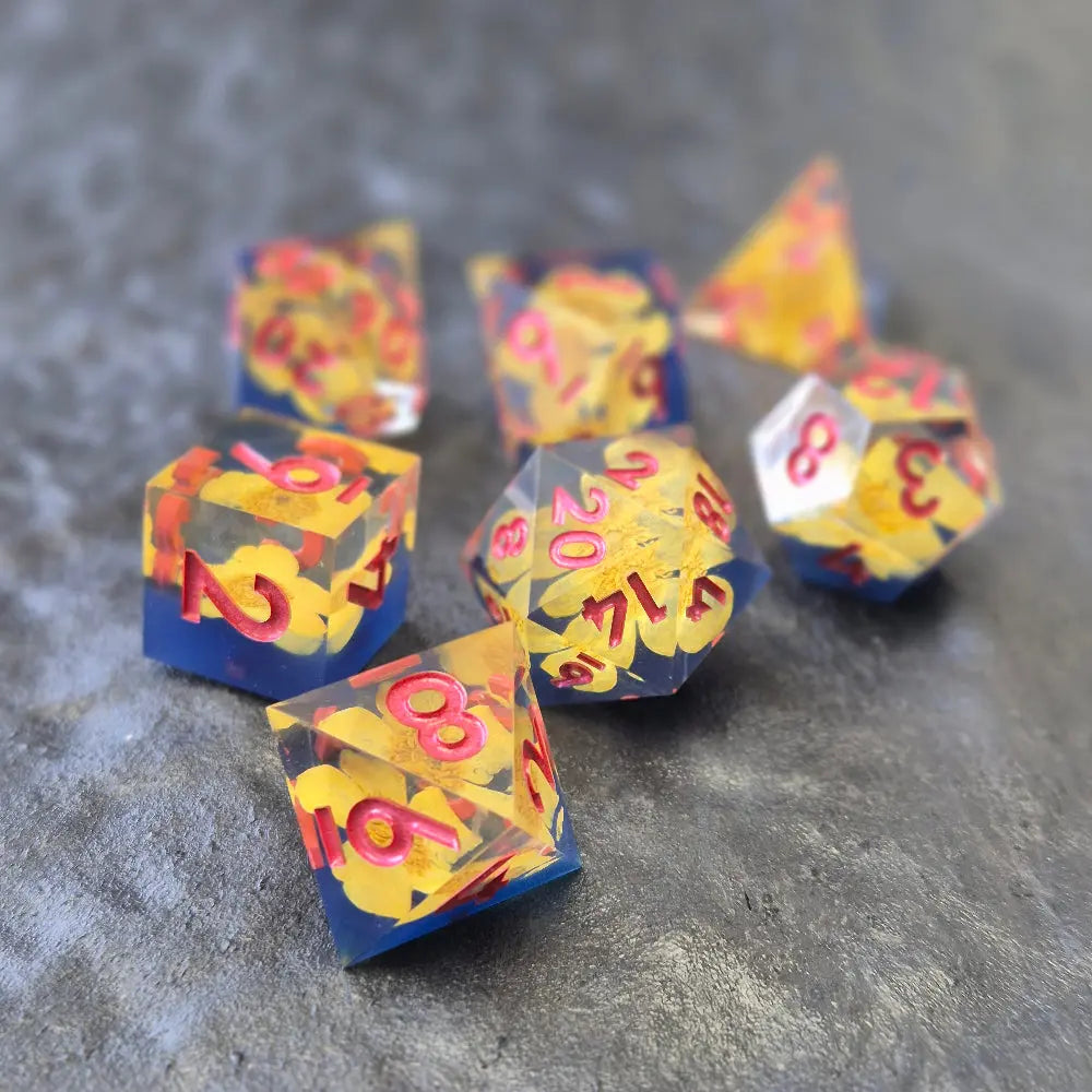 A set of clear sharp-edge resin dice with blue ground color and yellow flower inside on a black surface