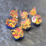 A set of clear sharp-edge resin dice with blue ground color and yellow flower inside on a black surface