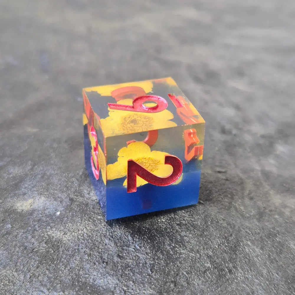 A set of clear sharp-edge resin dice with blue ground color and yellow flower inside on a black surface