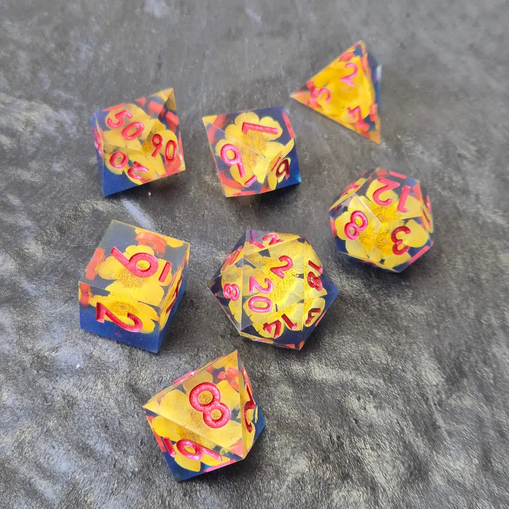 A set of clear sharp-edge resin dice with blue ground color and yellow flower inside on a black surface