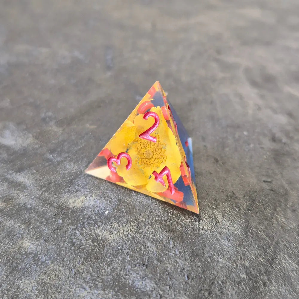 A set of clear sharp-edge resin dice with blue ground color and yellow flower inside on a black surface