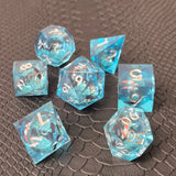 A set of clear light blue tinted liquid core dice with koi fish and glitters inside, displayed on a black textured surface