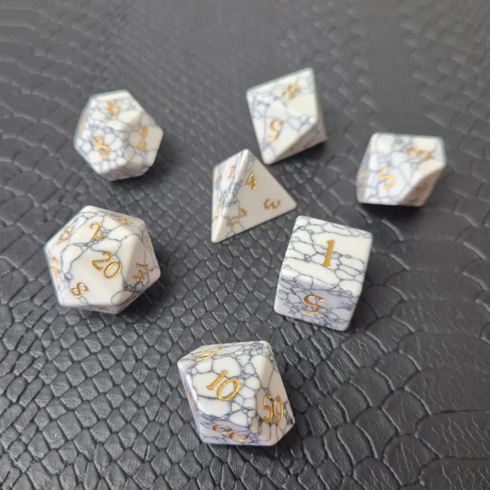 Set of white marble-textured gemstone dice with gold numbering, displayed on a black leather surface.