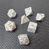 Set of white marble-textured gemstone dice with gold numbering, displayed on a black leather surface.