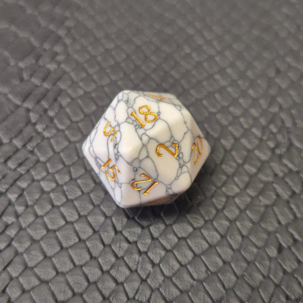 D20 white marble-textured gemstone die with gold numbering, displayed on a black leather surface.