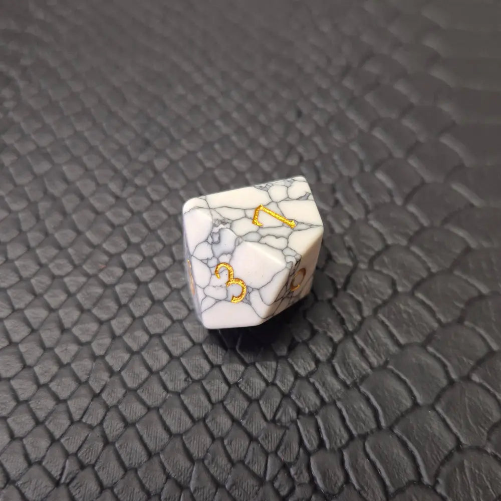 Set of white marble-textured gemstone dice with gold numbering, displayed on a black leather surface.