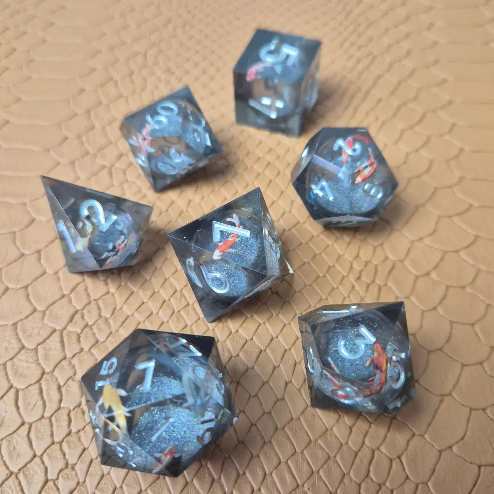 A set of clear grey tinted liquid core resin dice with koi fish inside filled with glitters on a beige textured surface