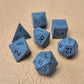 A set of matte black/ dark grey gemstone dice on a beige textured surface
