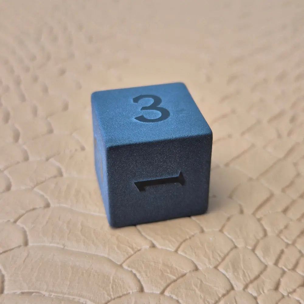A set of matte black/ dark grey gemstone dice on a beige textured surface