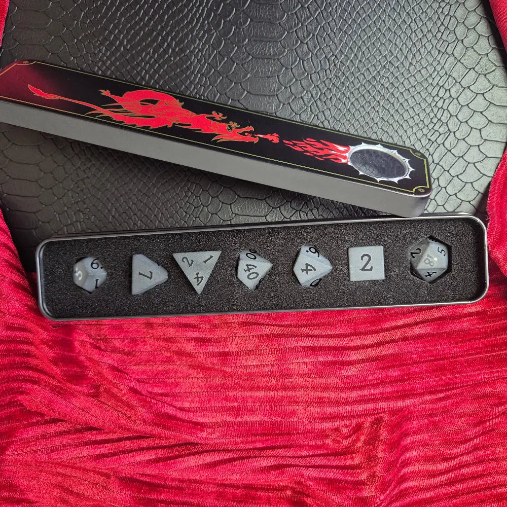 A set of matte black/ dark grey gemstone dice on a beige textured surface