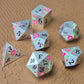 A set of silver metal dice with pink flowers and green stems and black numbers engraved, on a beige textured surface