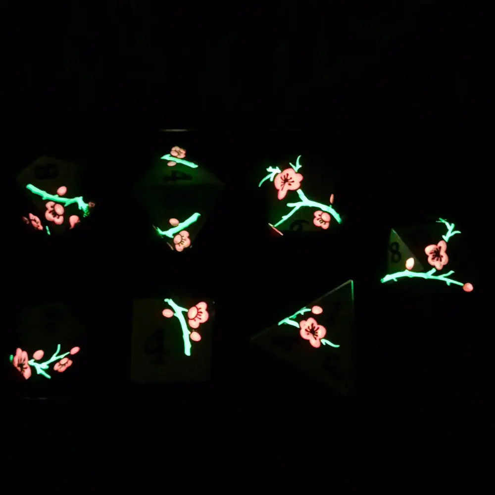 A set of silver metal dice with pink flowers and green stems and black numbers engraved, on a beige textured surface