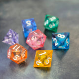 A set of rainbow coloured resin dice witch liquid core displayed on metal plate