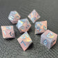 A set of pink sharp edge resin dice with blue numbers on a black textured surface