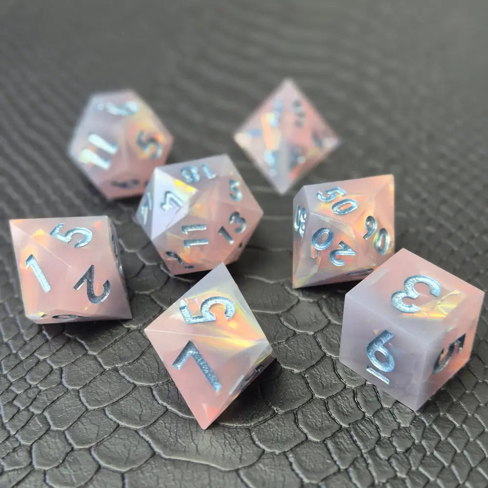 A set of pink sharp edge resin dice with blue numbers on a black textured surface