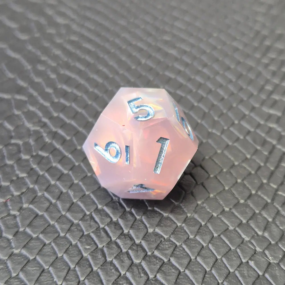 A set of pink sharp edge resin dice with blue numbers on a black textured surface