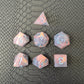 A set of pink sharp edge resin dice with blue numbers on a black textured surface